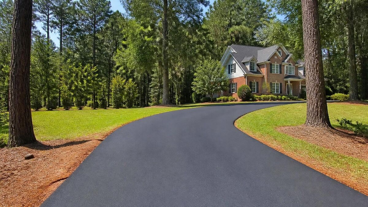 A freshly paved black asphalt driveway curving through tall pines up to a brick two-story home